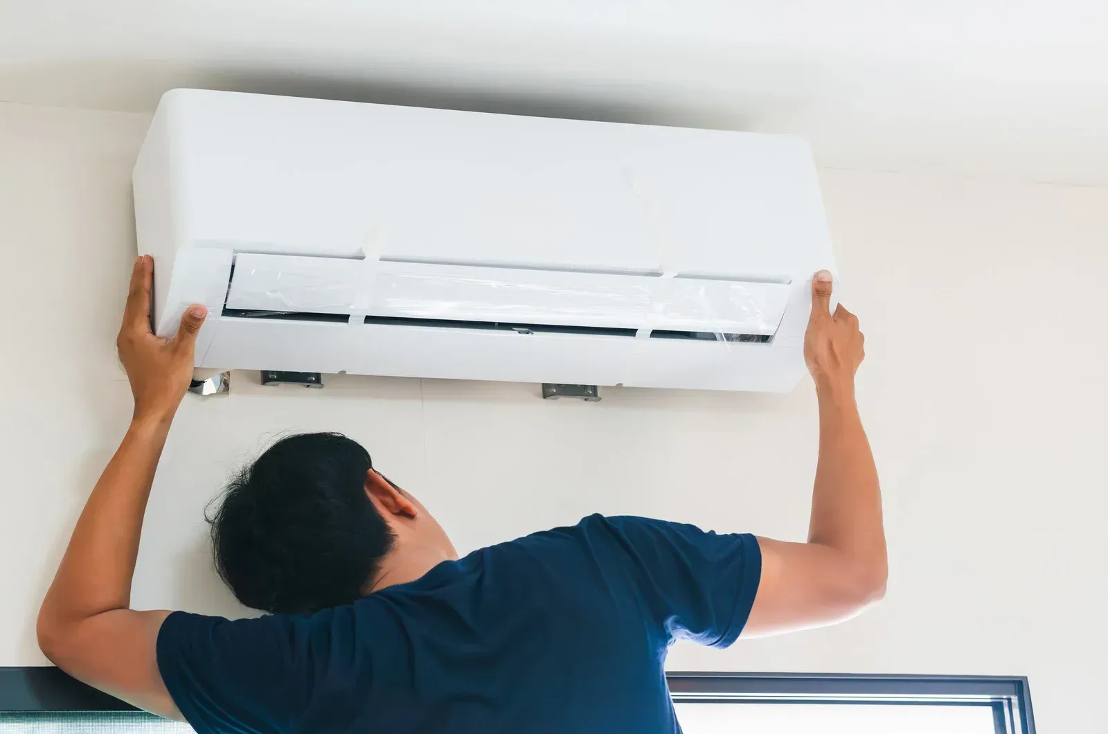Man installing or repairing a white air conditioning unit on a wall.