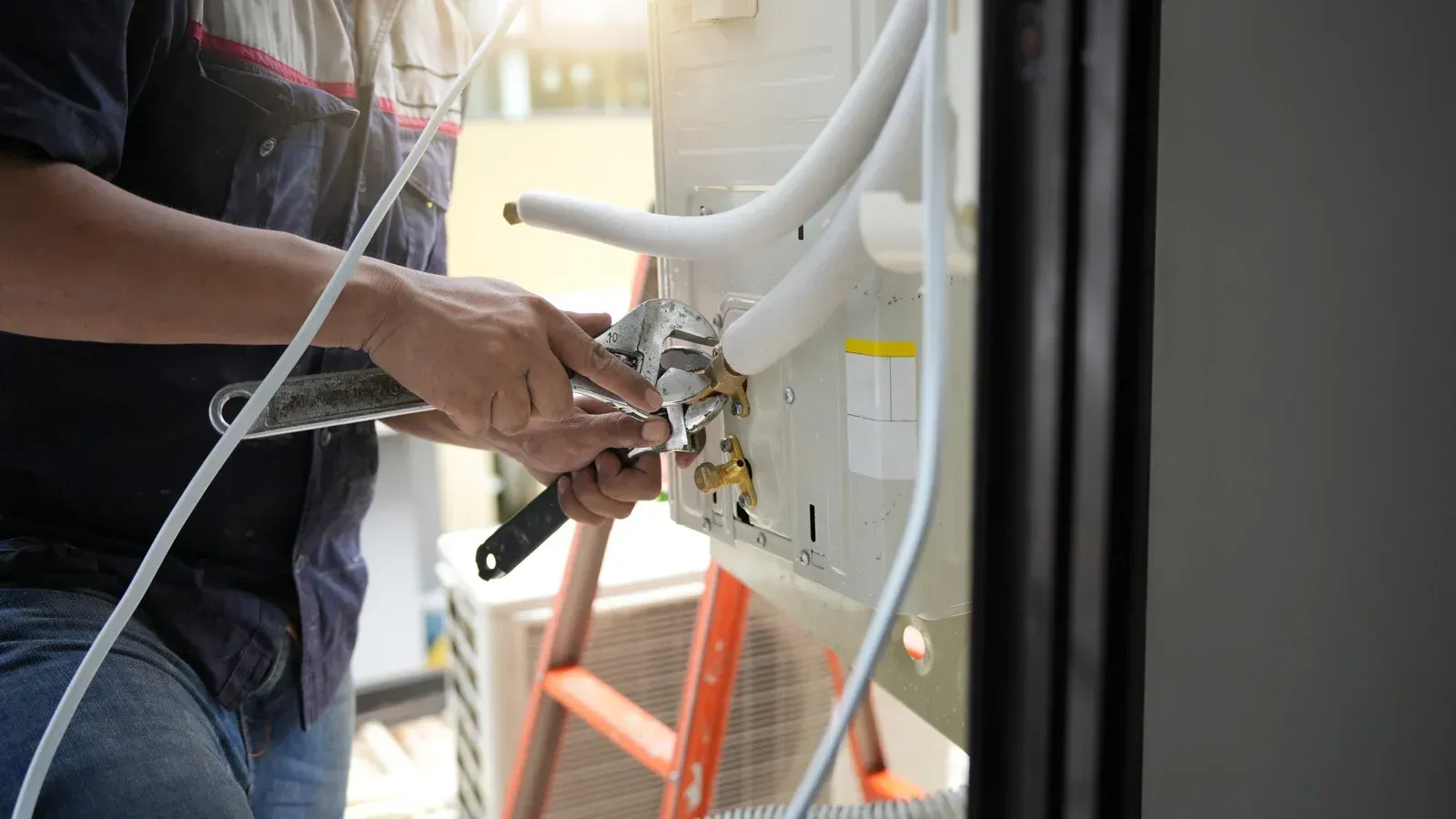HVAC technician using a wrench to repair an air conditioning unit outdoors.