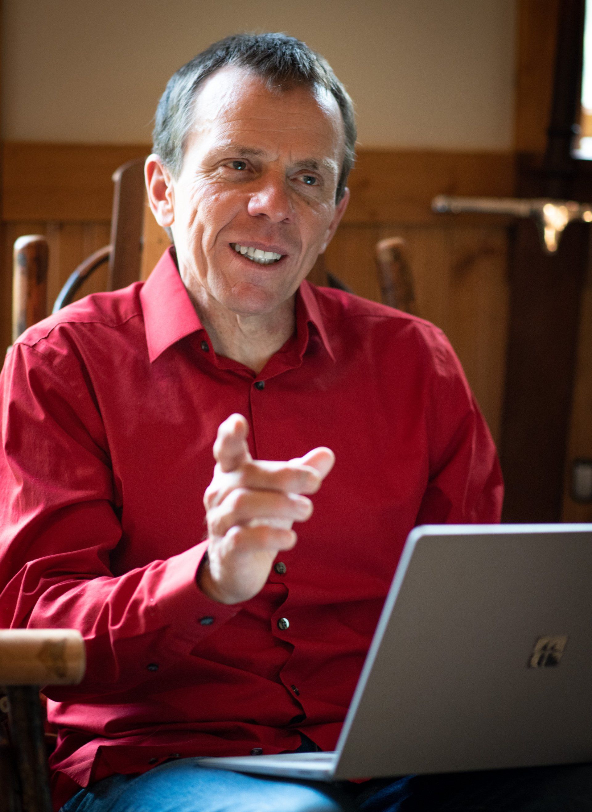 A man in a red shirt is sitting in a chair using a laptop computer.