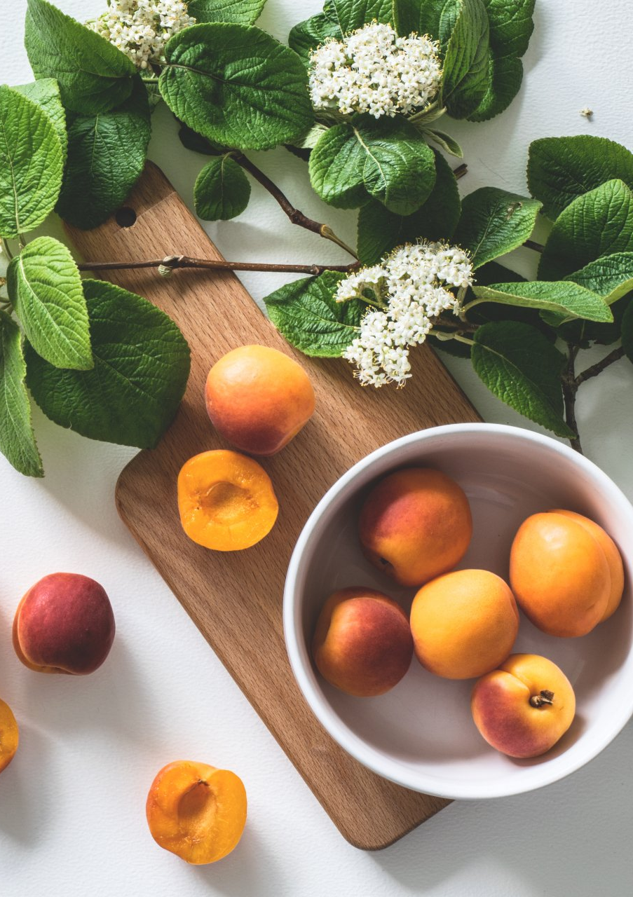 A bowl of apricots is sitting on a wooden cutting board.