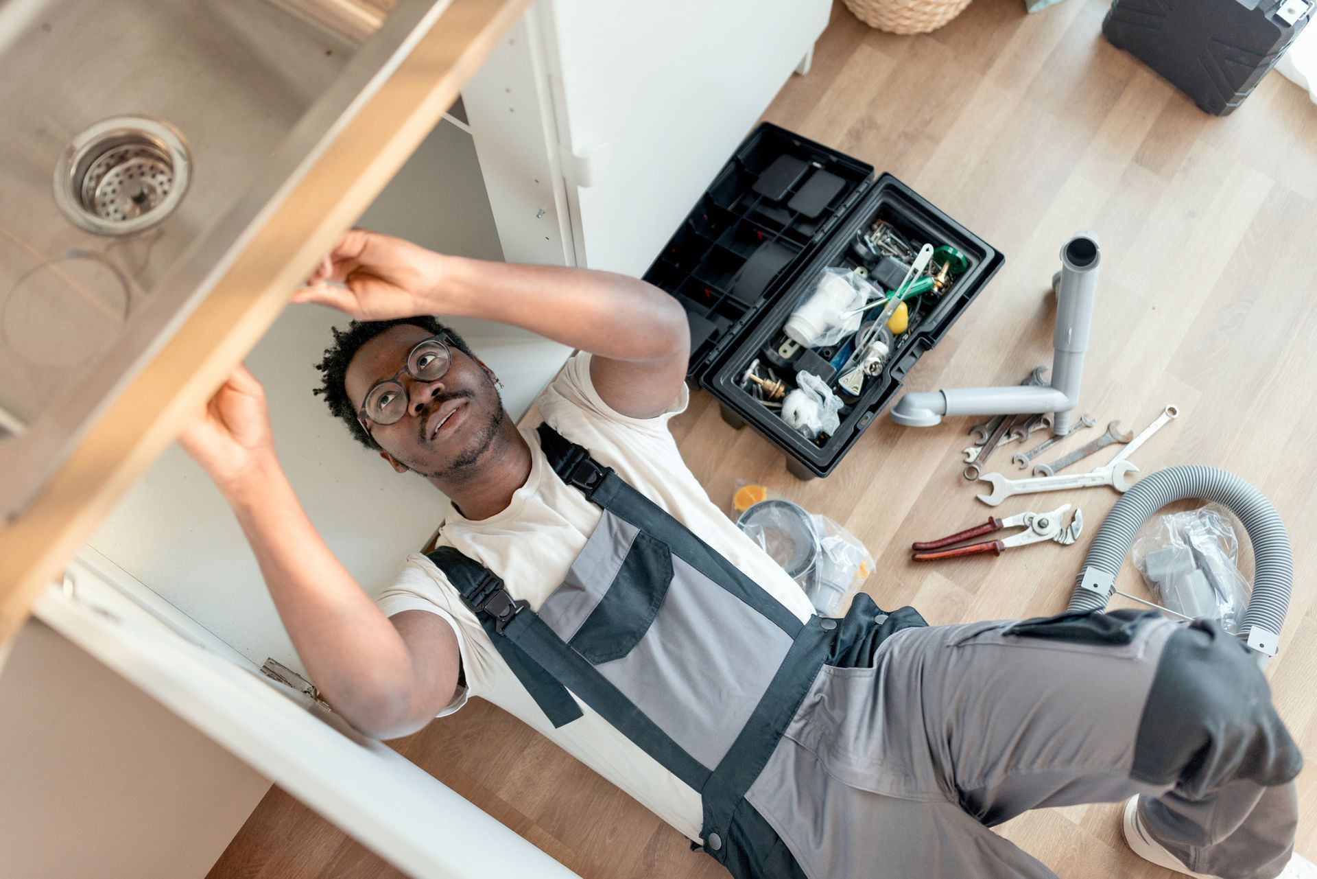 Plumber fixing a leak in the kitchen sink of a house.