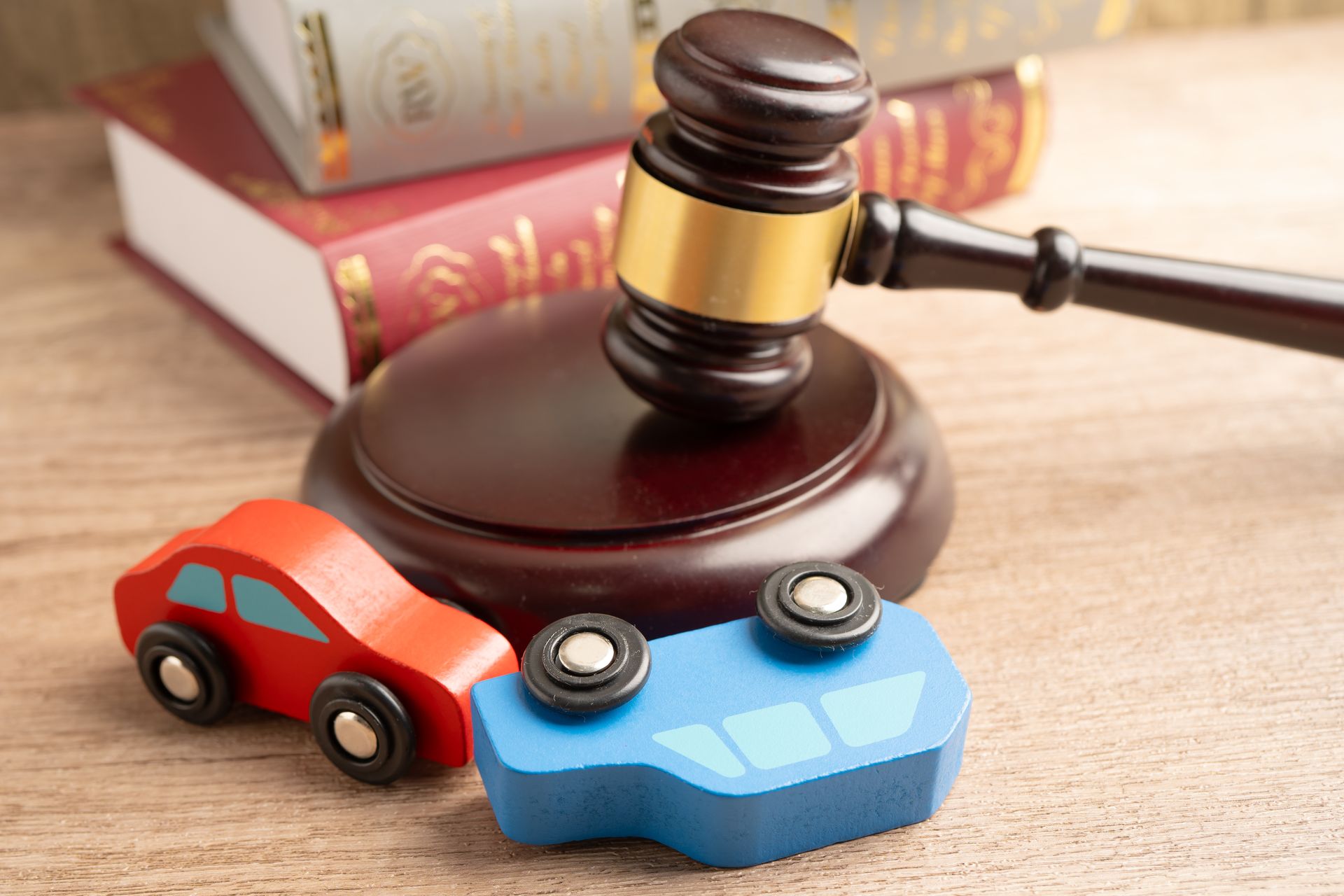 Wooden toy cars, one overturned, beside a judge’s gavel and law books, symbolizing car accident law.