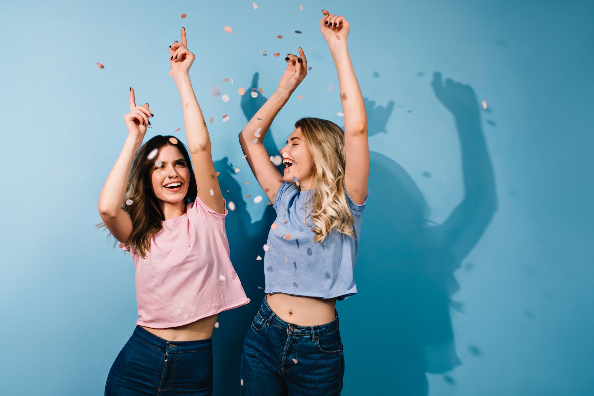 Two people in casual clothes smiling and cheering with confetti against a light blue background.