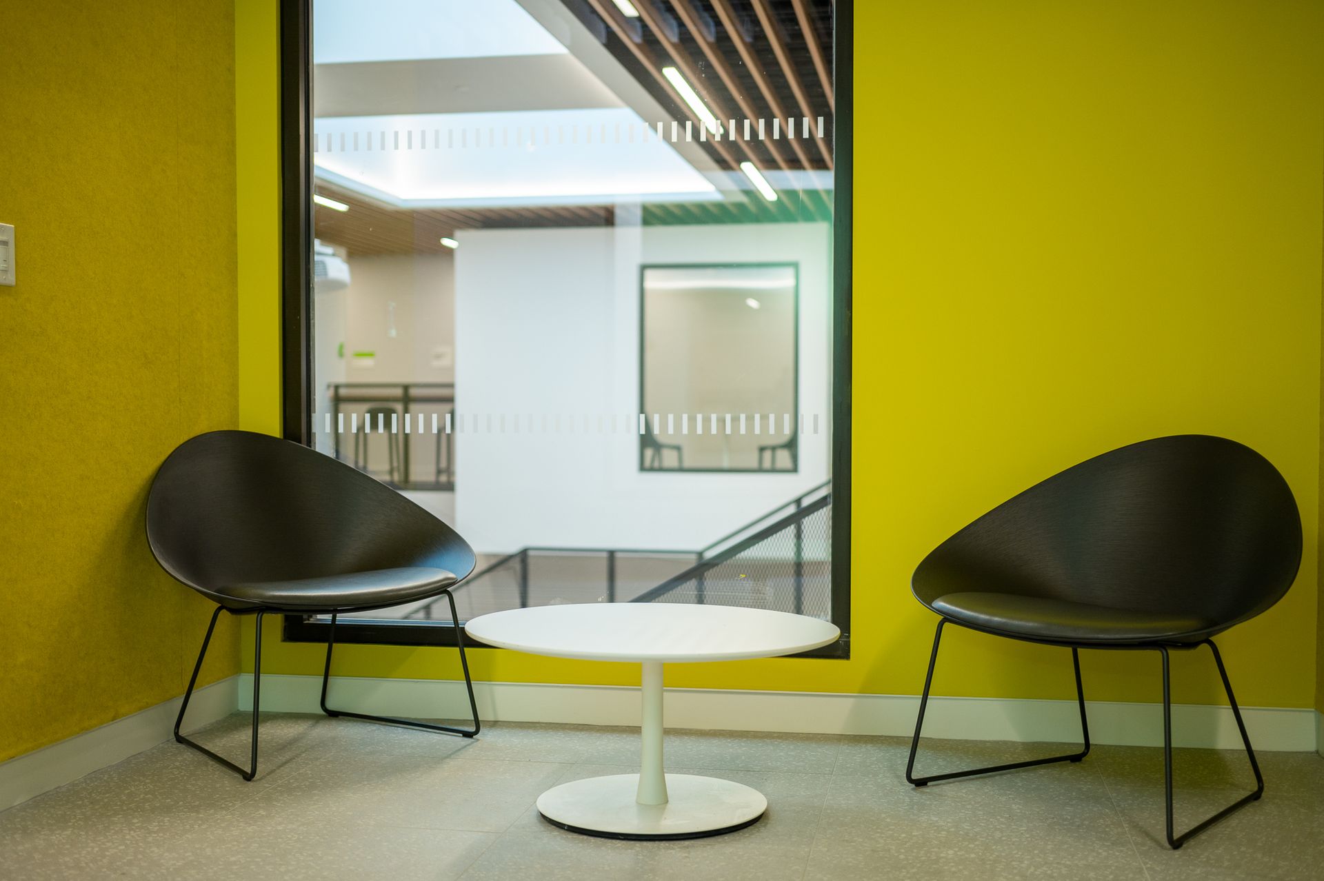 Two black chairs facing each other with a small round white table between them against bright yellow walls.