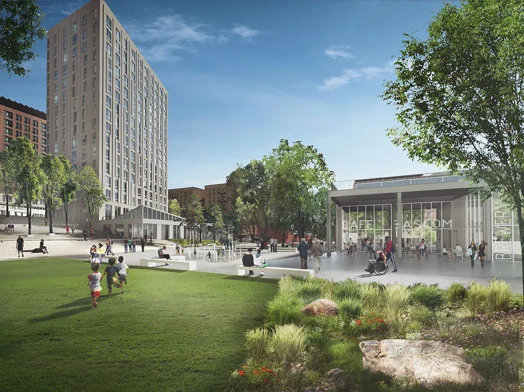 A tall modern apartment building overlooks a sunny park with a grassy lawn, walking paths, and a glass-walled pavilion.