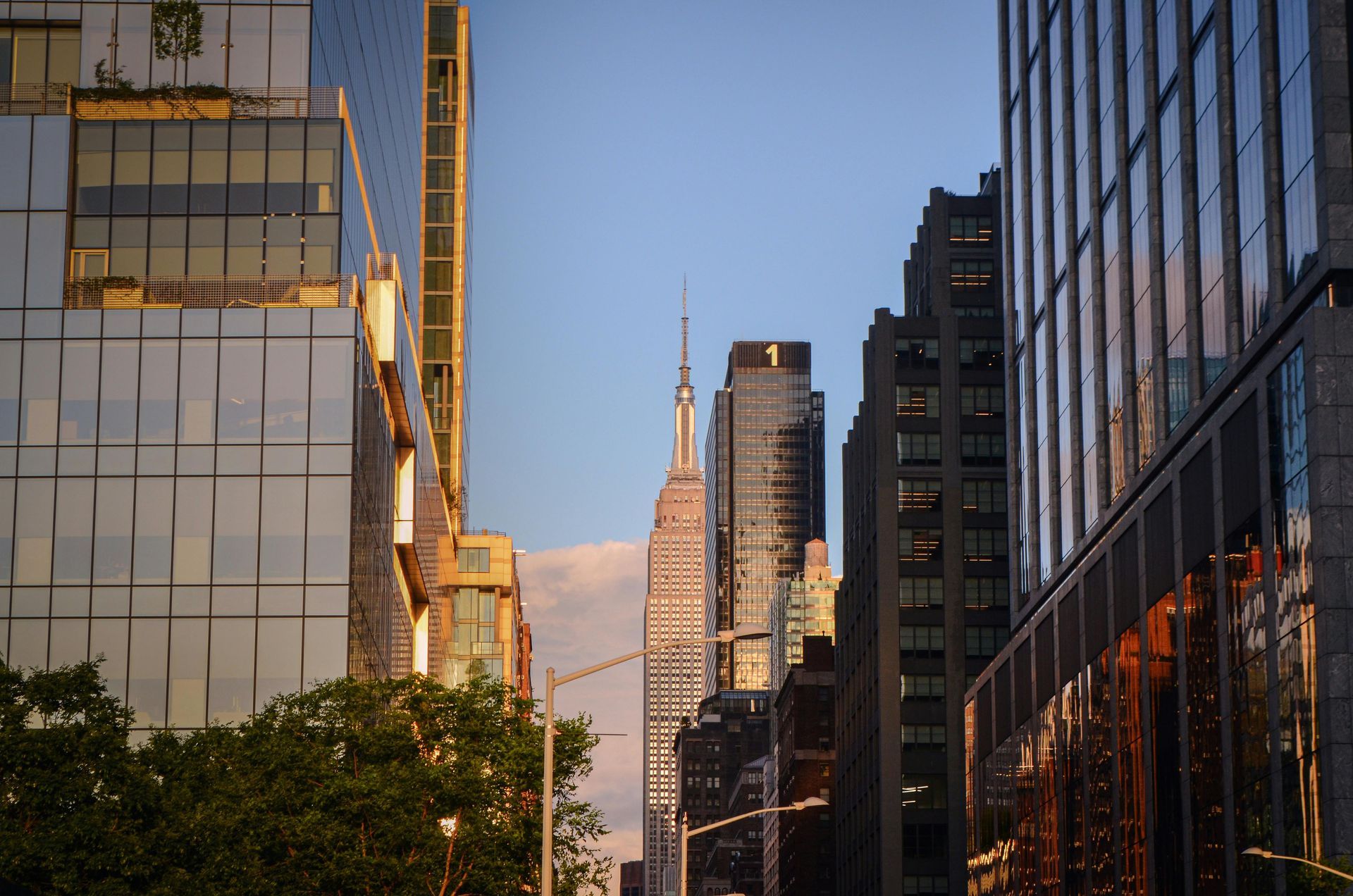 The Empire State Building stands framed between modern glass skyscrapers during sunset in a bustling city.