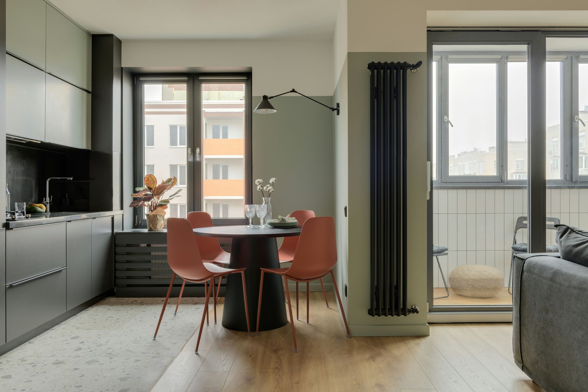 A modern kitchen and dining area with matte black cabinets, a round table with terracotta chairs, and a tall radiator.