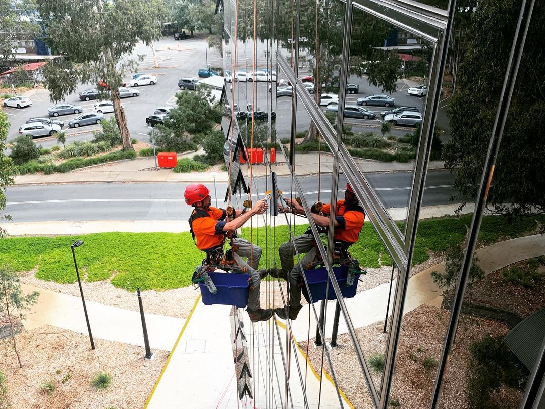 Two rope access specialists are climbing a very tall building.