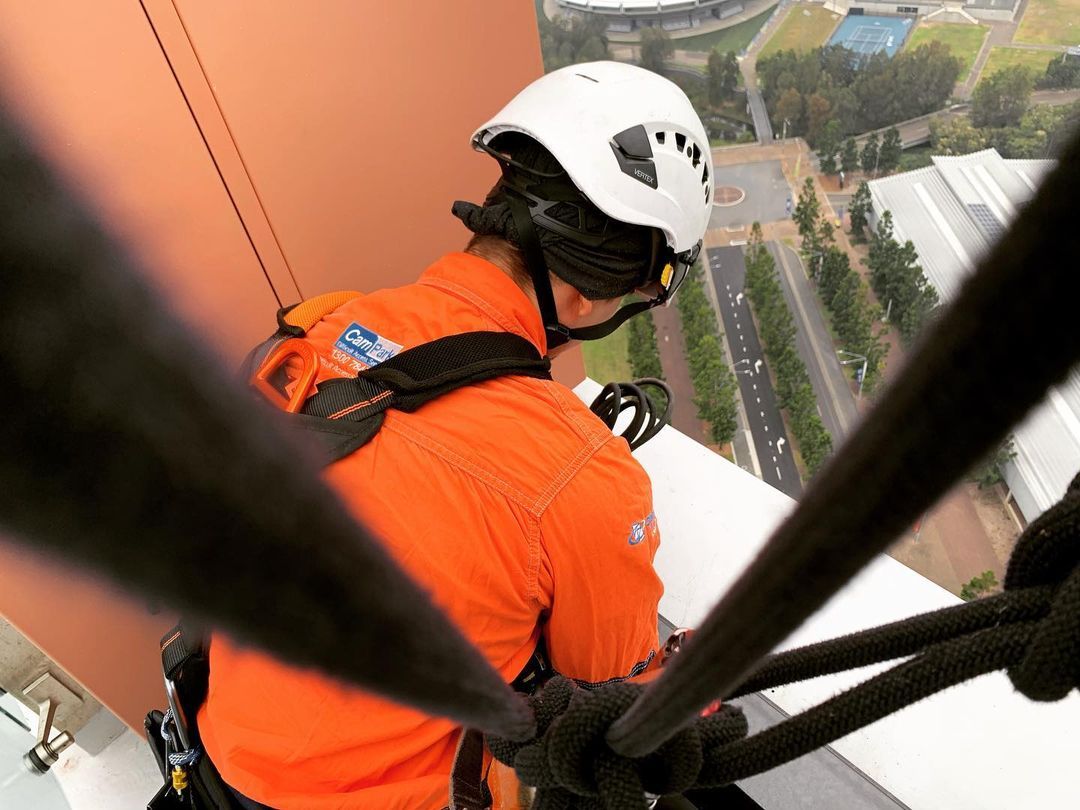 A man wearing a helmet and an orange shirt is climbing a building.
