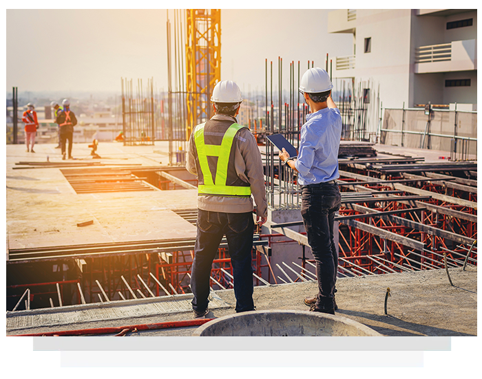 Two construction workers in hard hats reviewing plans on a building rooftop.