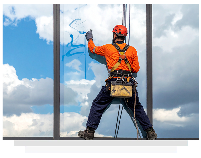 man removing graffiti on a glass surface using rope access