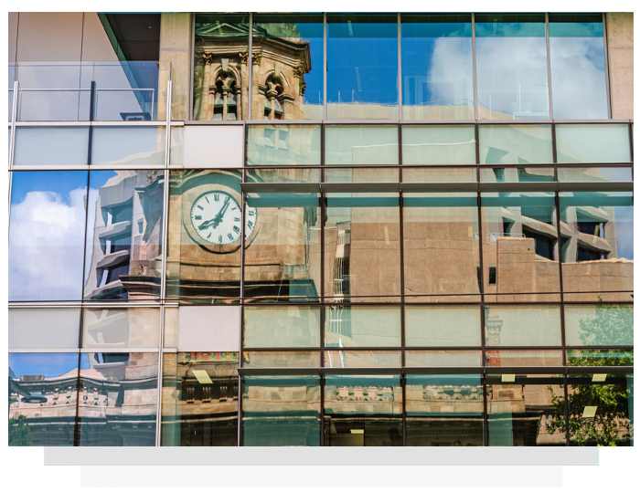 Reflection in glass facade: clock tower, blue sky, modern building.