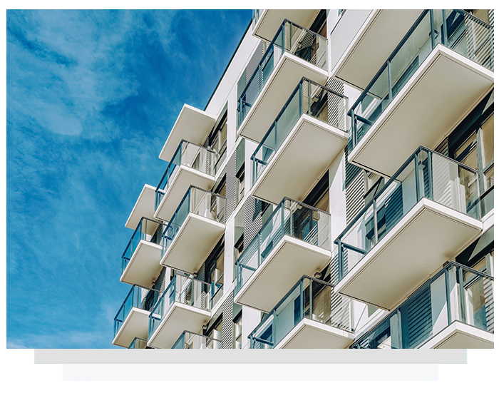 Modern white apartment building with balconies against a bright blue sky.