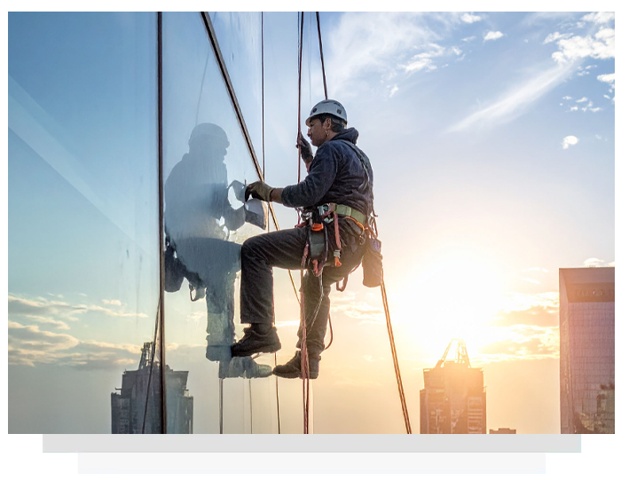 man applying protective coatings on a glass surface of a high-rise using rope access