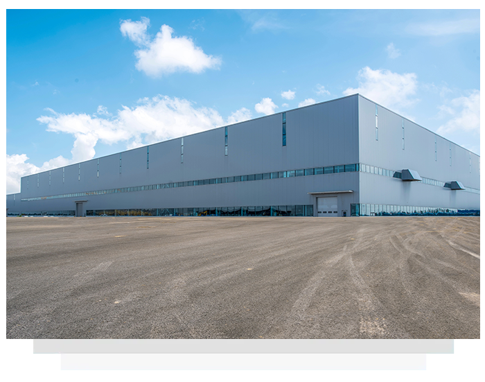 Large gray industrial building against a blue sky, asphalt parking lot.