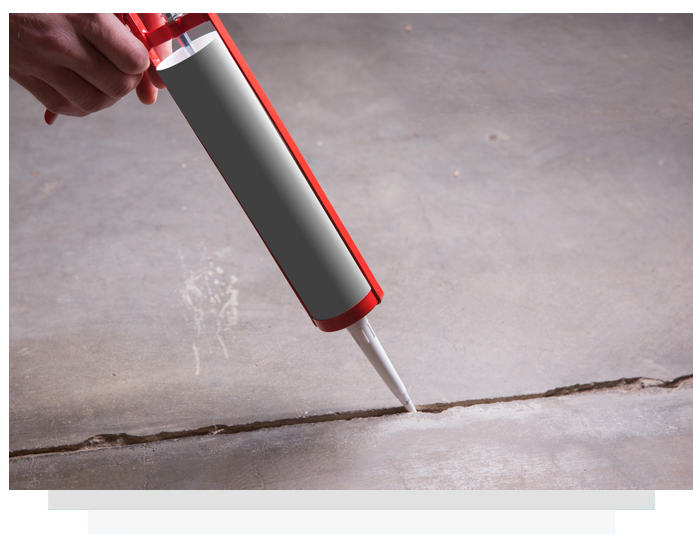Hand using a caulking gun to apply sealant into a crack on a concrete surface.