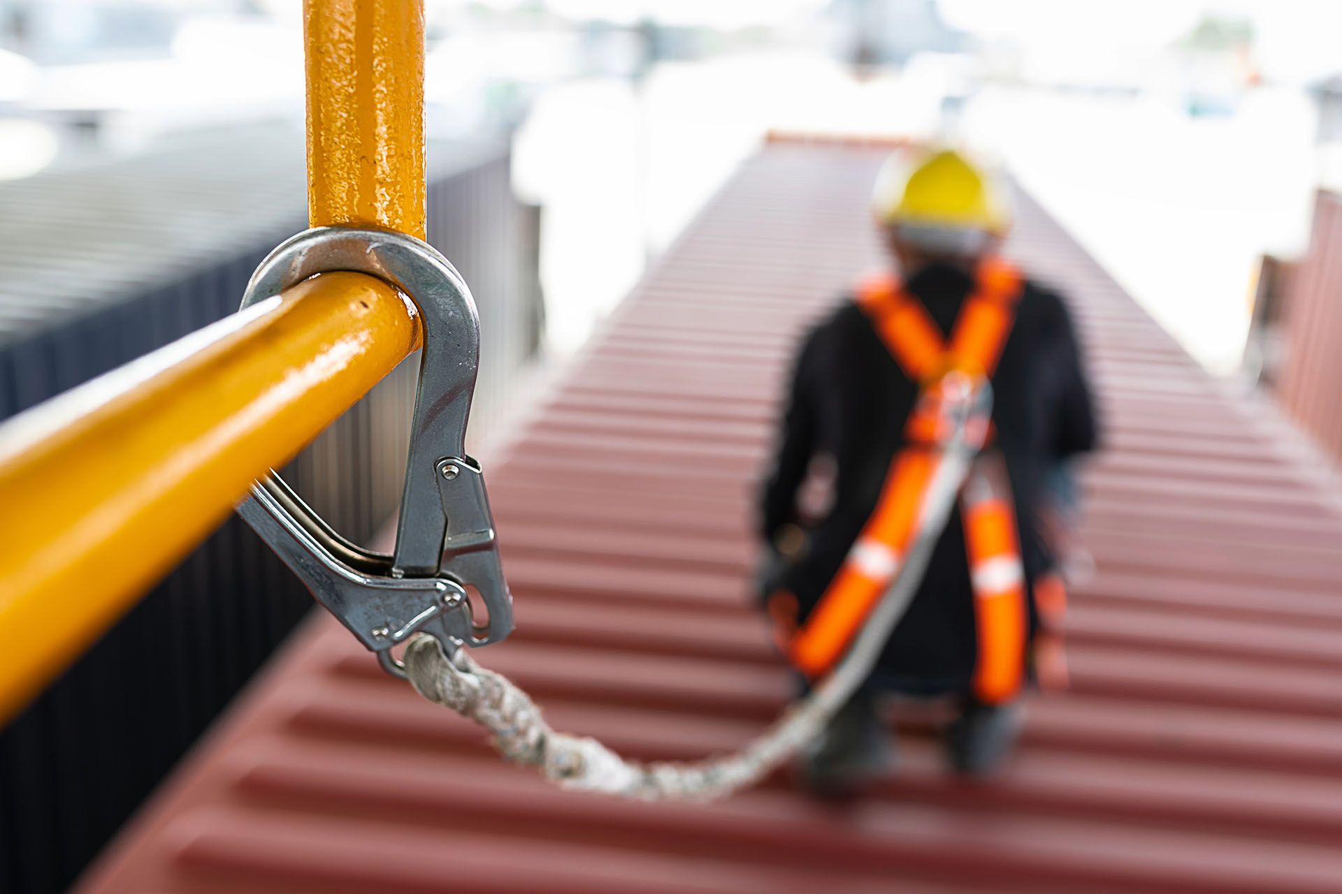 Worker in safety harness attached to a rail on top of shipping container.