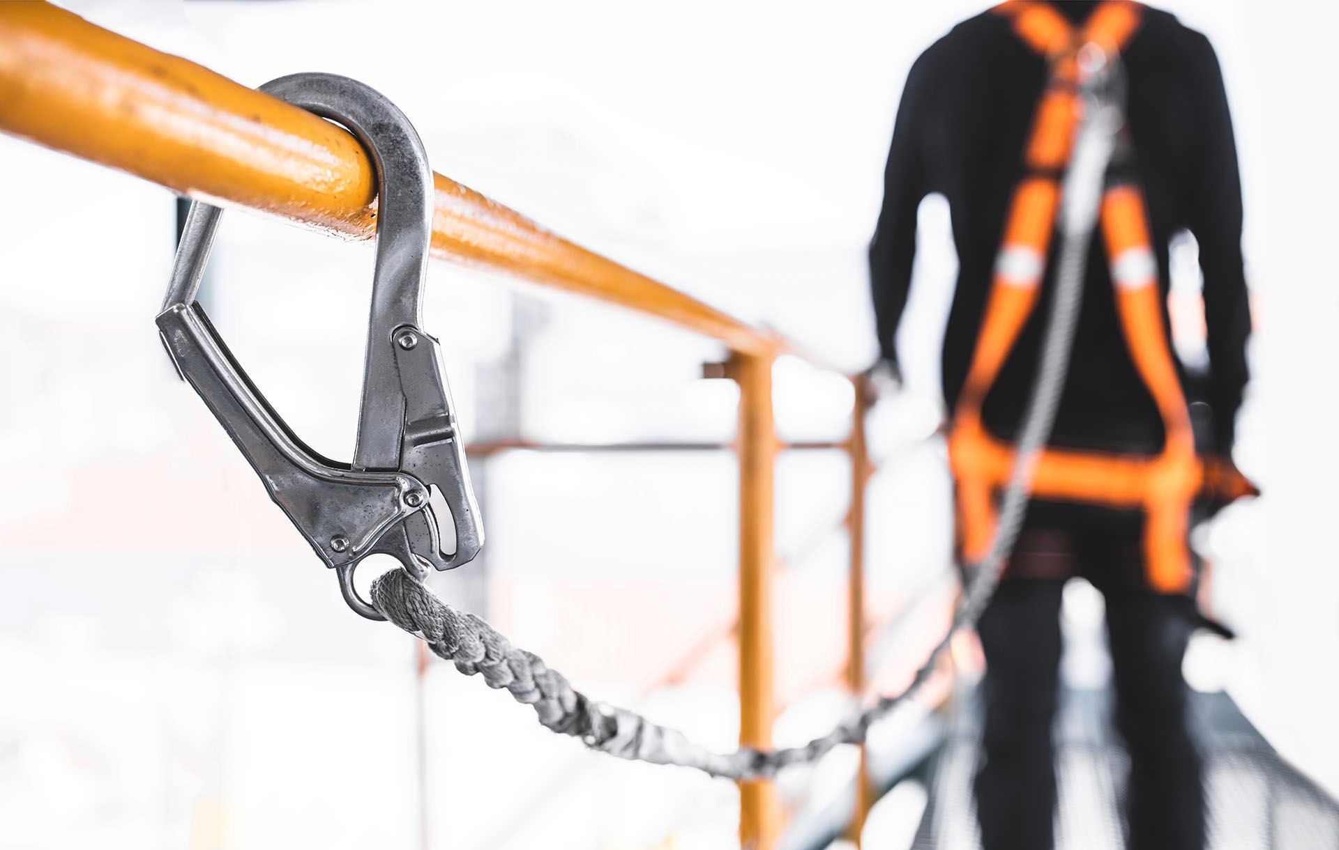 Fall protection hook attached to orange railing with worker in safety harness.