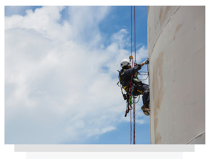 Rope access worker suspended beside a tall building against a blue sky