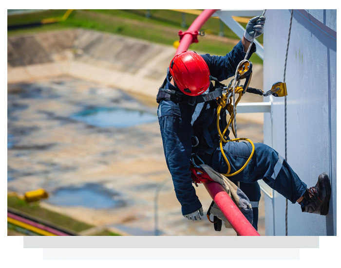 Worker in red helmet rappelling down a building wall with safety harness and rope
