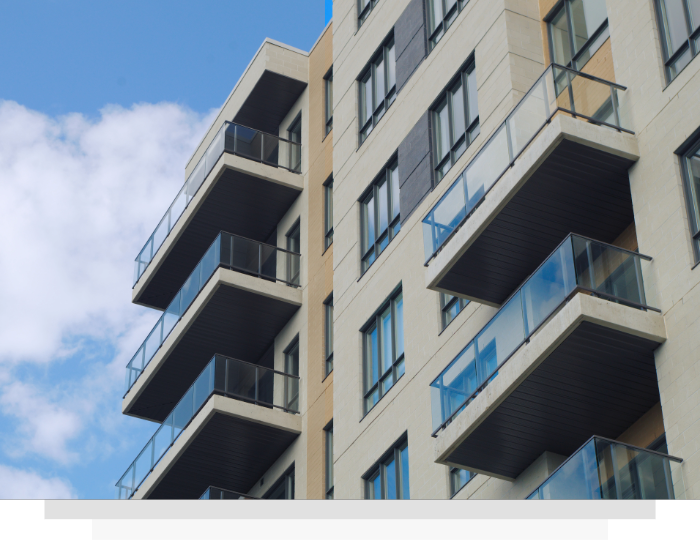 Modern apartment building with beige walls and glass-railed balconies against a blue sky