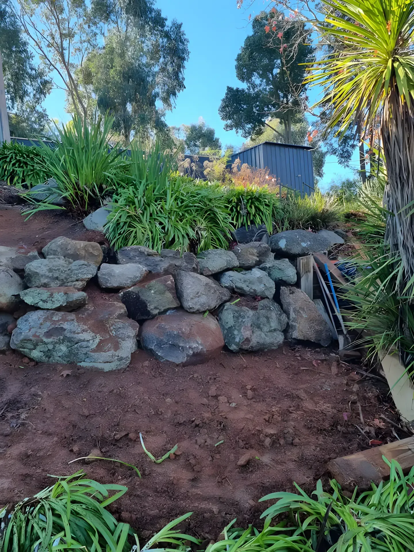 A rock wall in a garden with a shed in the background. — Grants Excavations In Osbornes Flat, VIC
