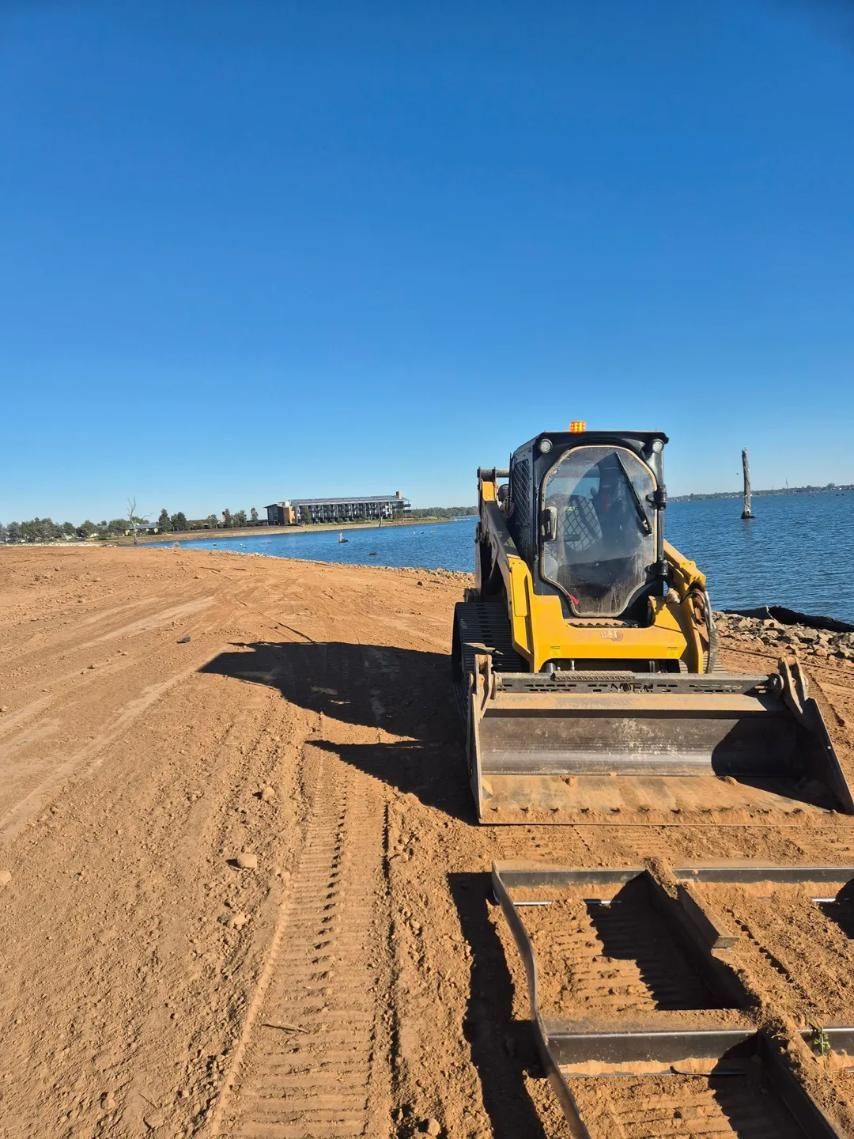 A Yellow Bulldozer Is Sitting On A Dirt Road Next To A Body Of Water — Grants Excavations In Osbornes Flat, VIC