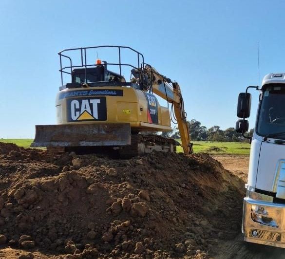 A Cat Excavator Sits On Top Of A Pile Of Dirt Next To A Truck — Grants Excavations In Osbornes Flat, VIC