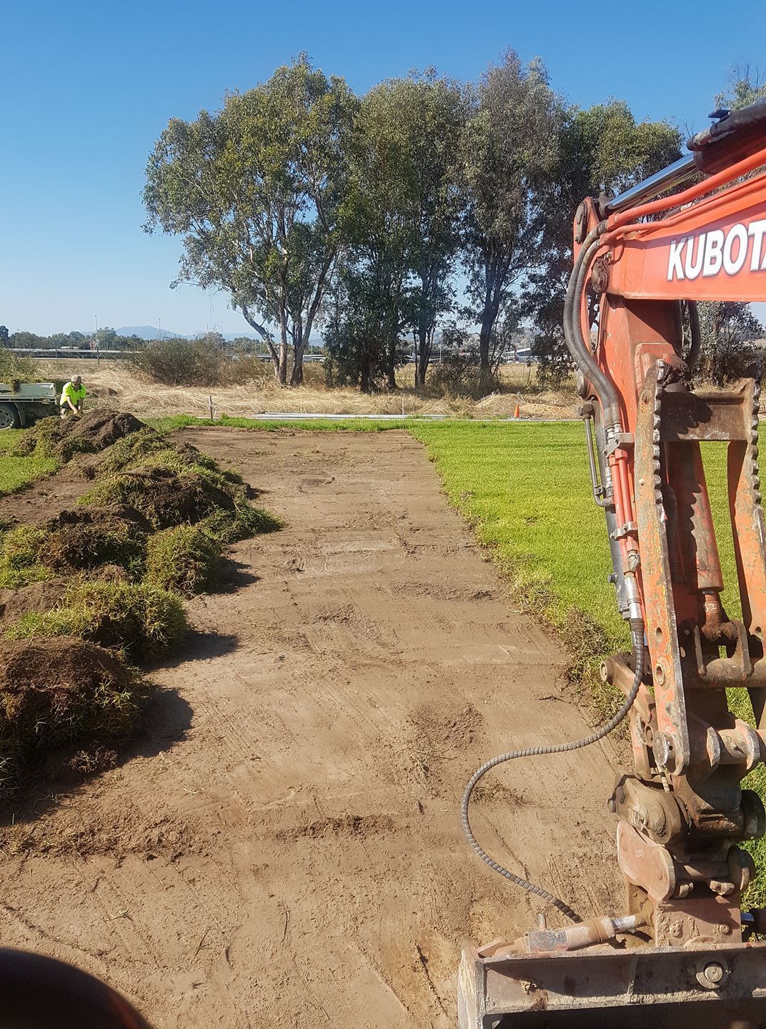 A Large Orange Excavator Is Working On A Dirt Road In A Field — Grants Excavations In Osbornes Flat, VIC