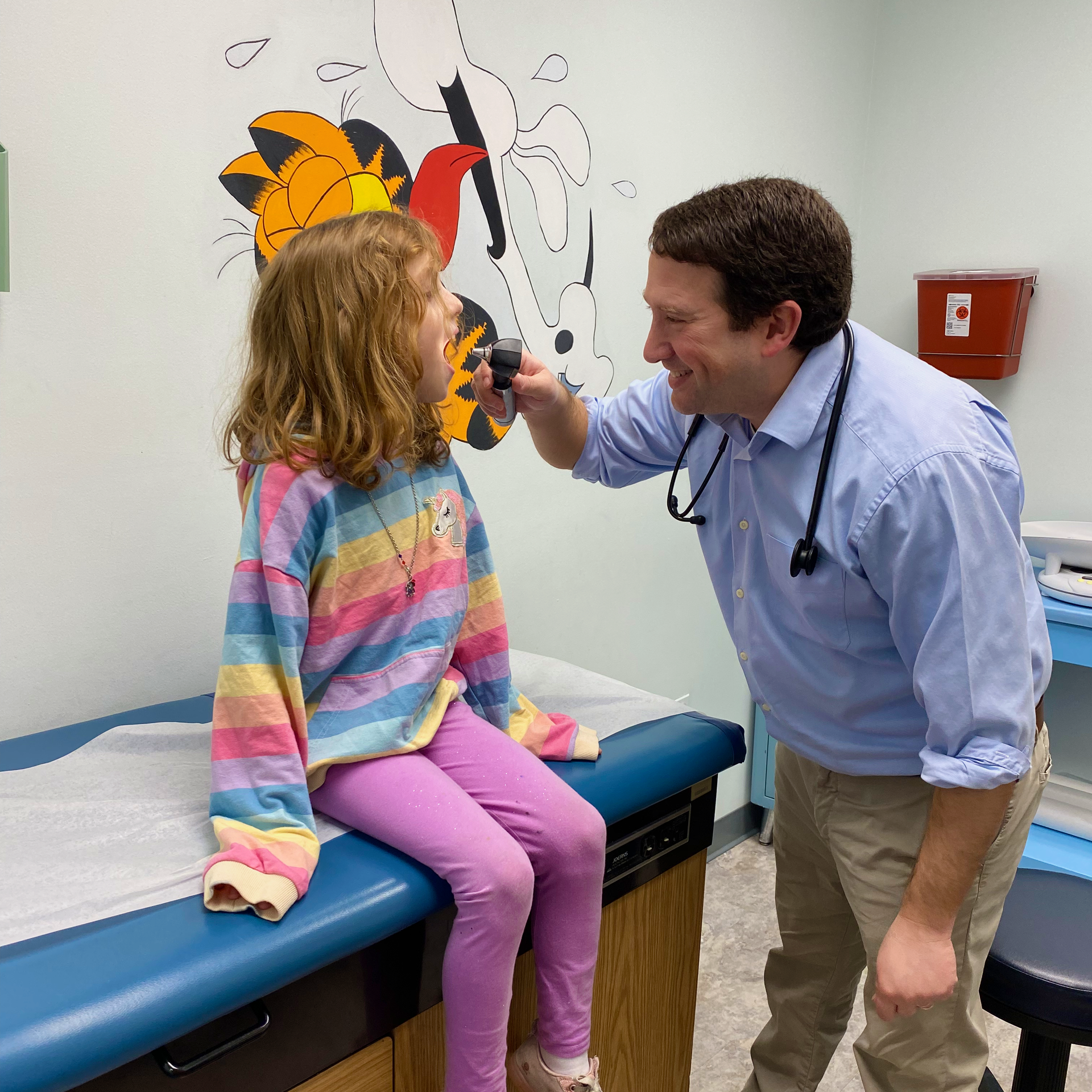 A pediatrician is examining a girl's mouth on a medical examination table.