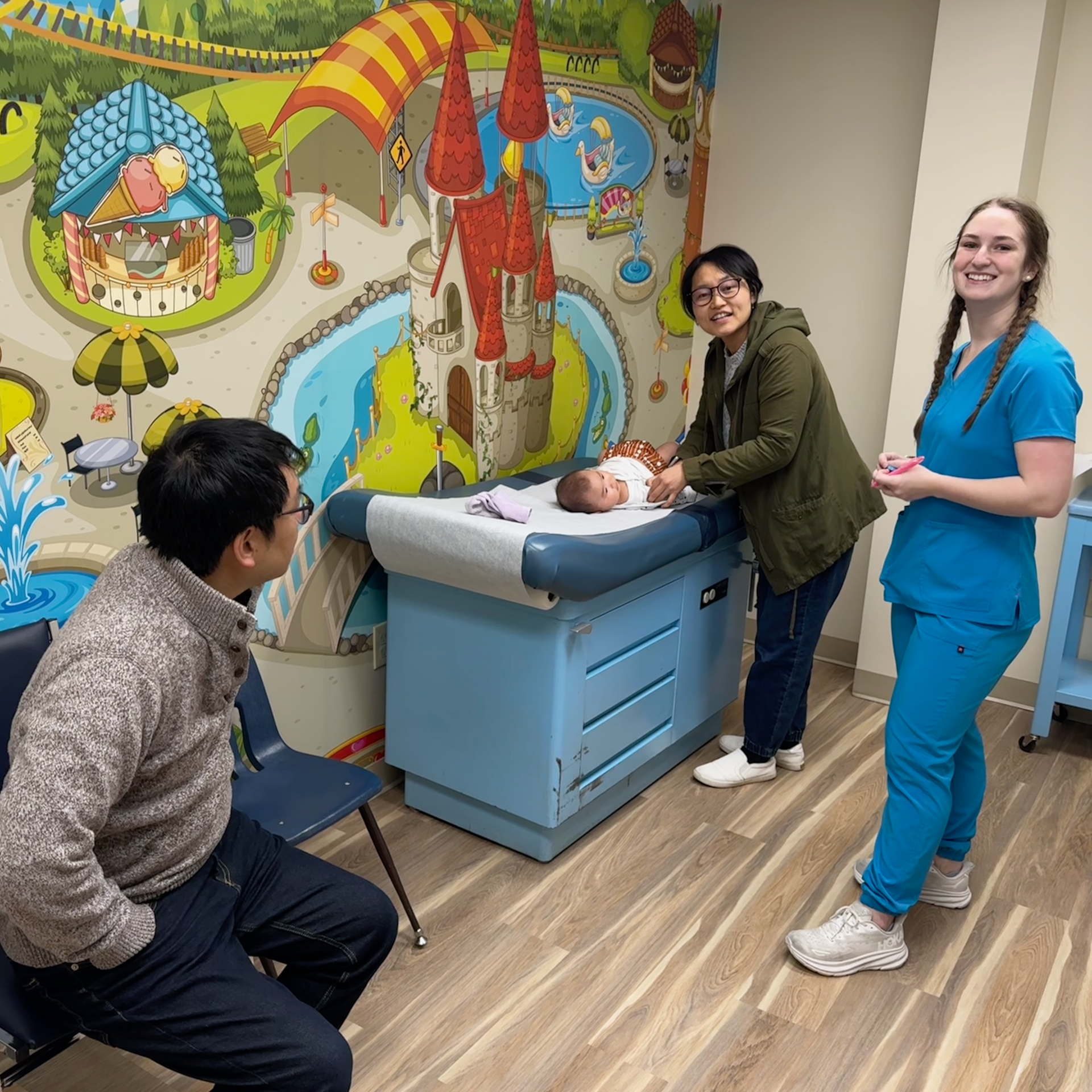 A group of people are standing around an examination table with a baby on it.