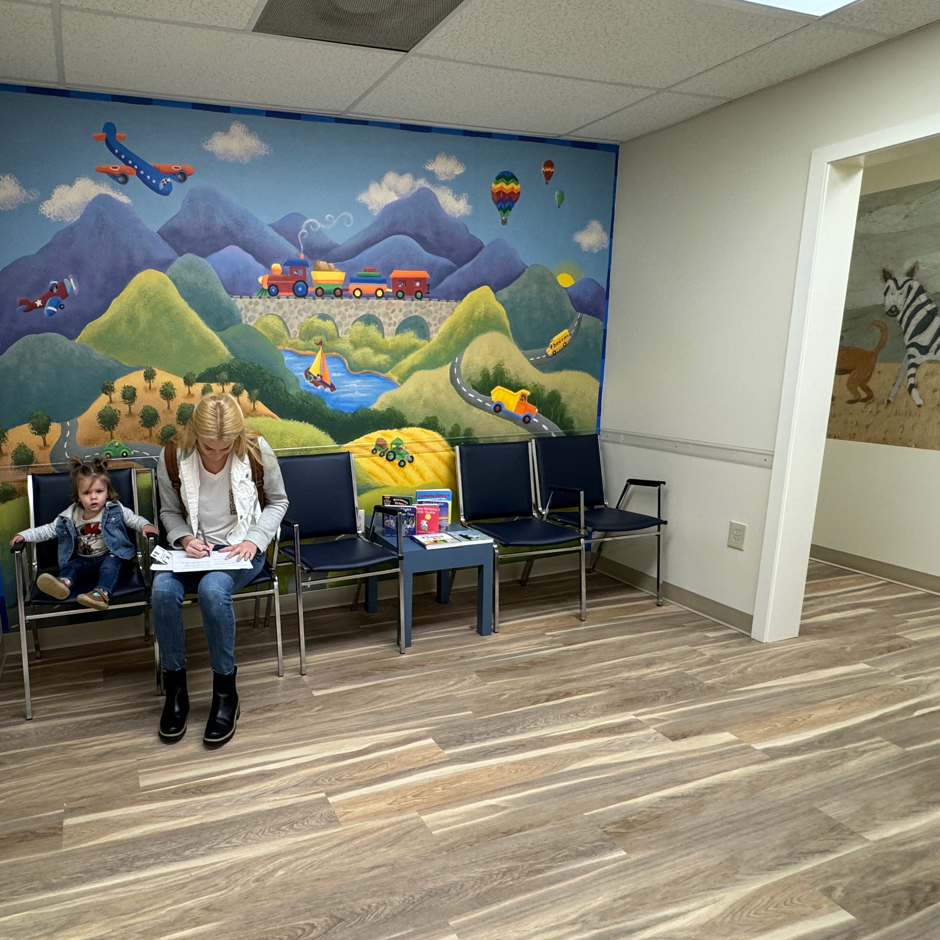 A woman and child are sitting in a waiting room with a painting on the wall