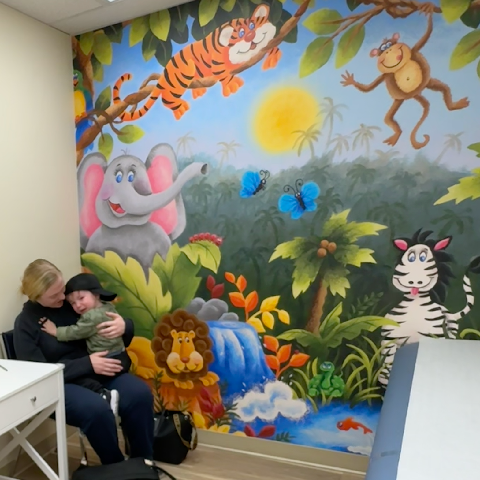 A woman holding a baby in front of a mural of animals