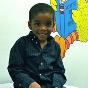 A young boy is sitting in front of a wall mural with a bird and book that says how to be a bird