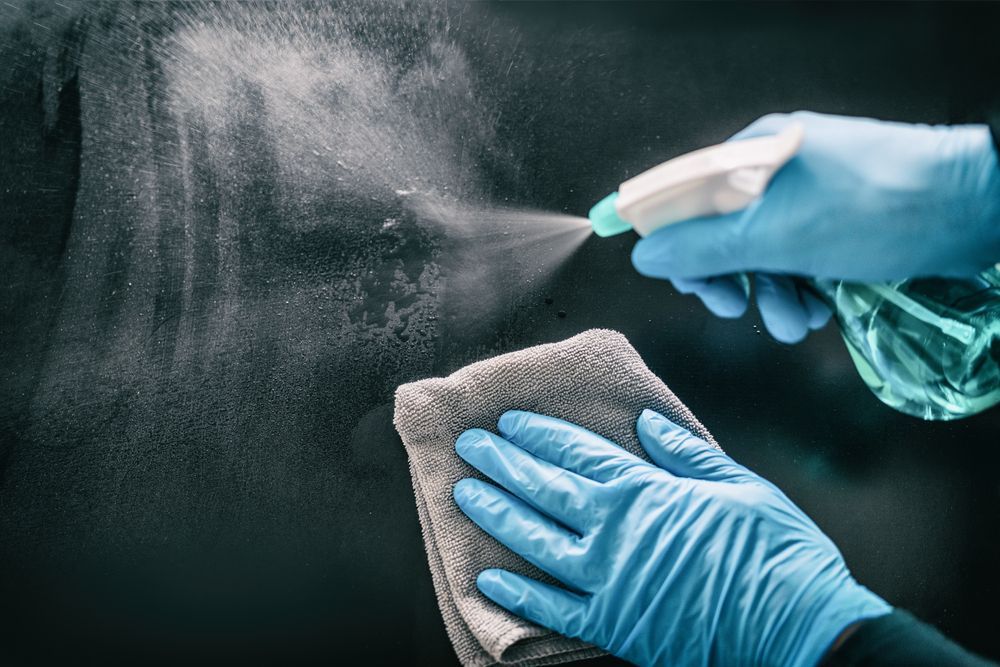 A person wearing blue gloves is spraying a cloth with a spray bottle.