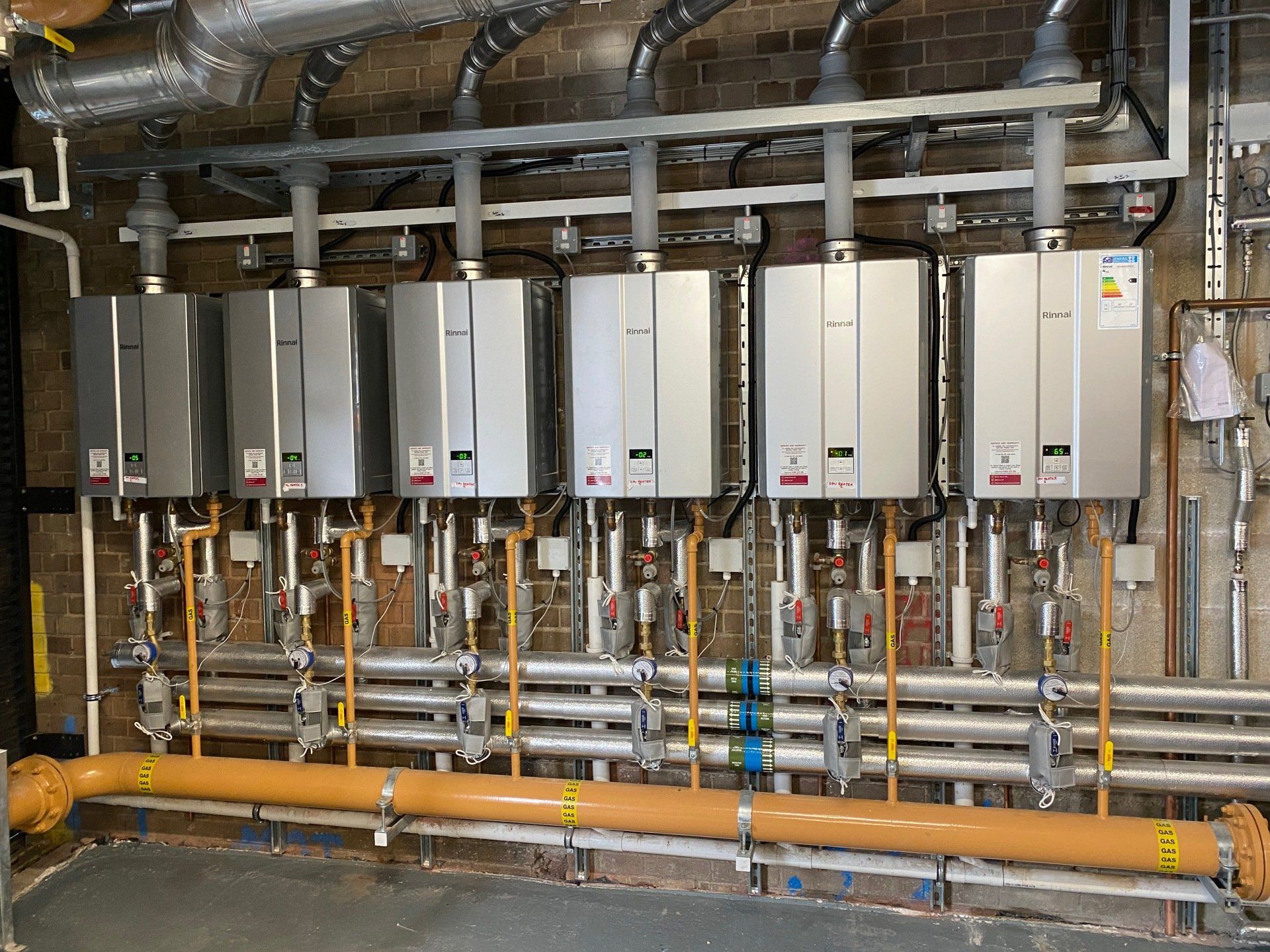 a row of water heaters are lined up on a wall next to pipes .