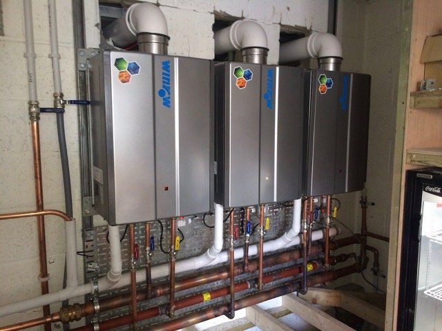 three water heaters are lined up in a room with copper pipes .