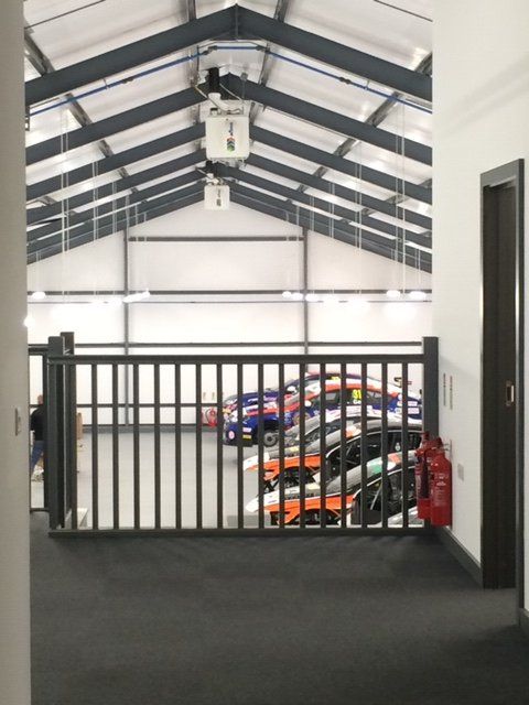 A hallway with cars parked behind a fence and a fire extinguisher on the floor