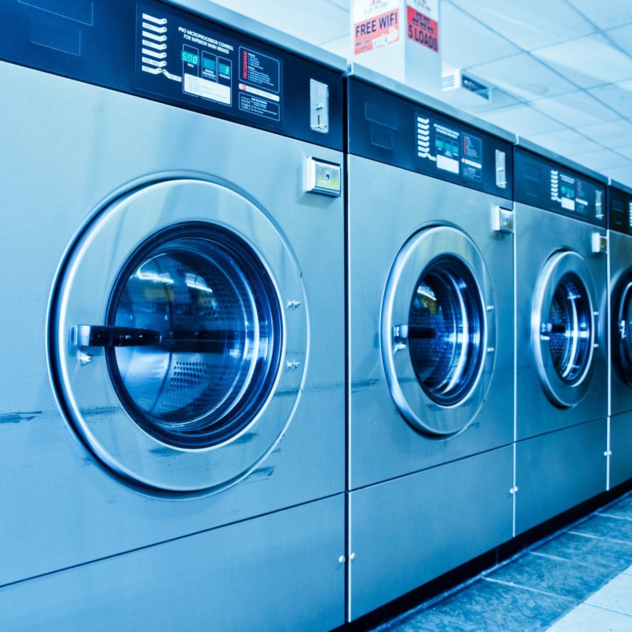 A row of stainless steel washing machines in a laundromat