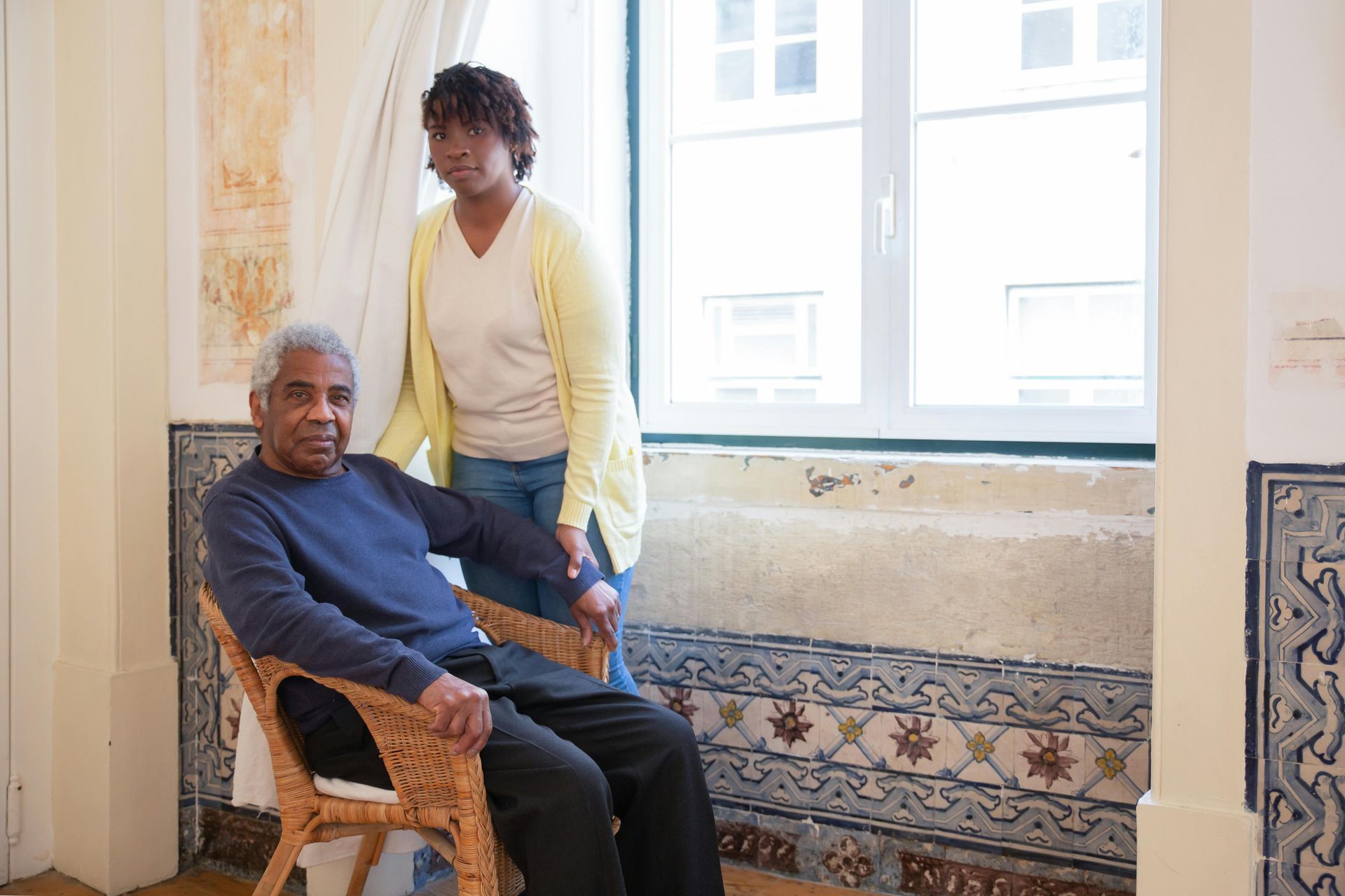 A woman is standing next to an older man sitting in a chair.