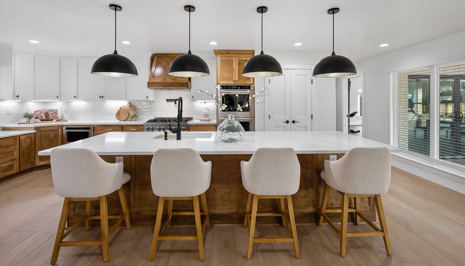 Modern kitchen with a long island, four light-colored stools, white countertops, and four black pendant lights above.