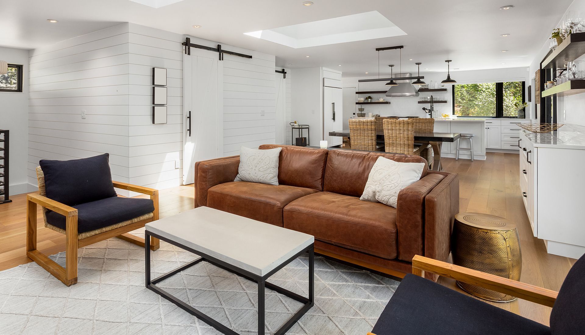 Living room with a brown leather sofa, two black armchairs, and a concrete coffee table on a white patterned rug.