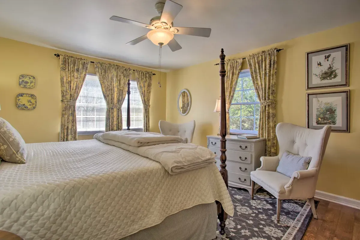 a bedroom with a four poster bed , chair , dresser and ceiling fan .