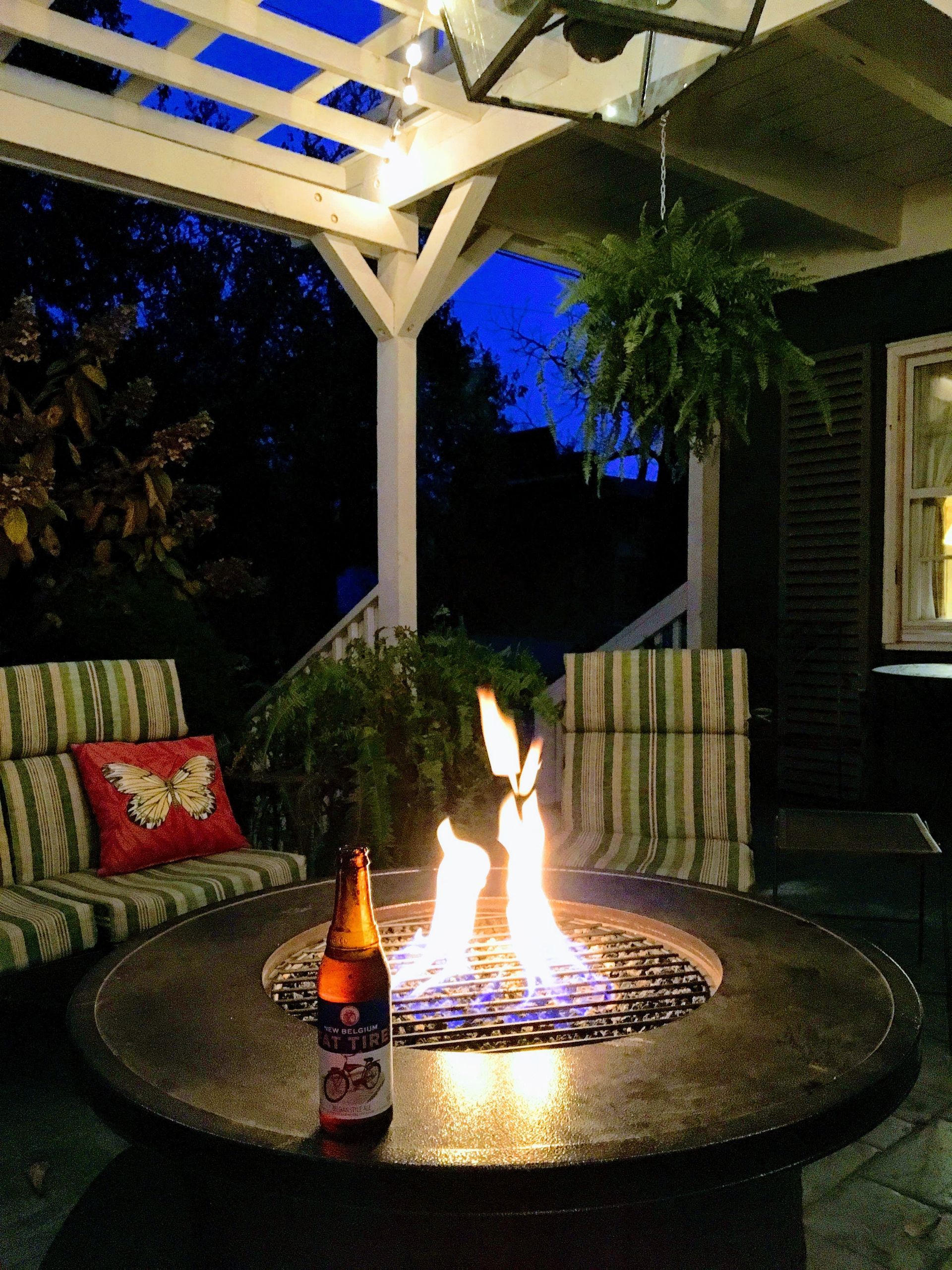 A bottle of beer sits on a table in front of a fire pit