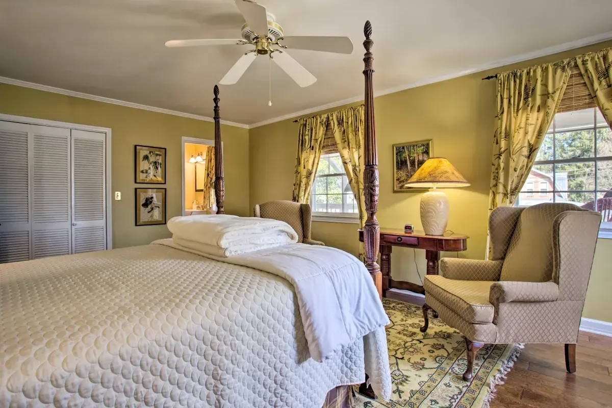a bedroom with a four poster bed , chair , desk and ceiling fan .