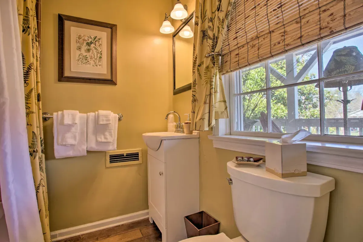a bathroom with a toilet , sink , mirror and window .