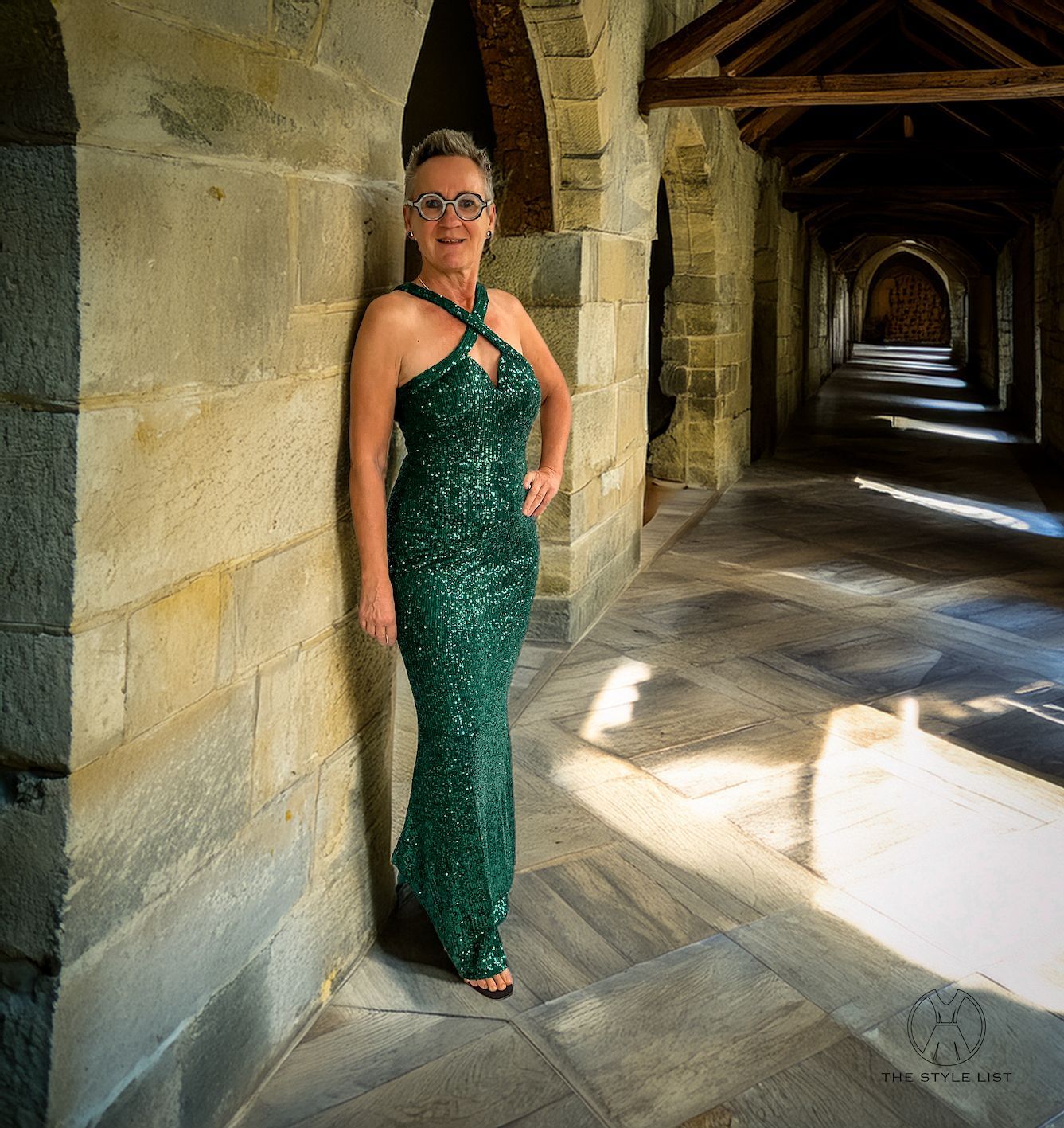 A woman in a green sequined dress leans against a stone wall