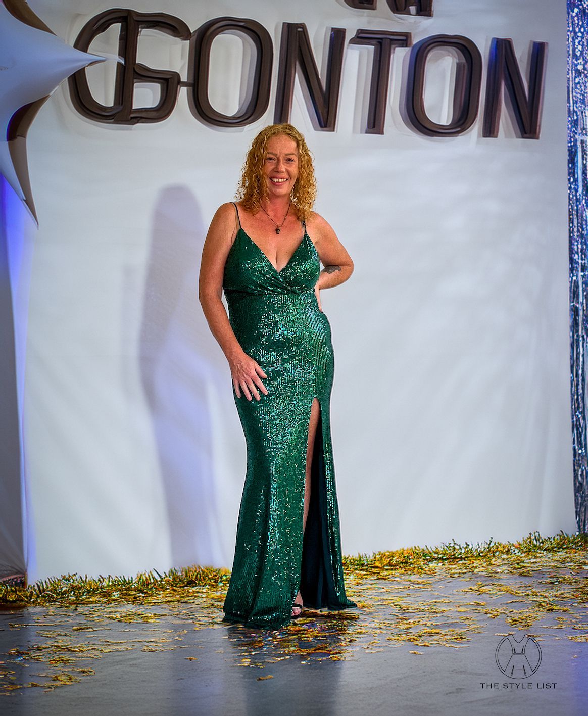A woman in a green sequined dress is standing in front of a sign that says gonton.
