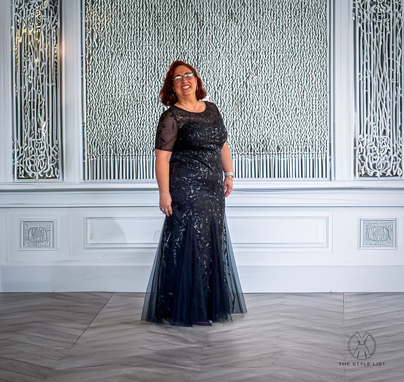 A woman in a black dress is standing in front of a wall.