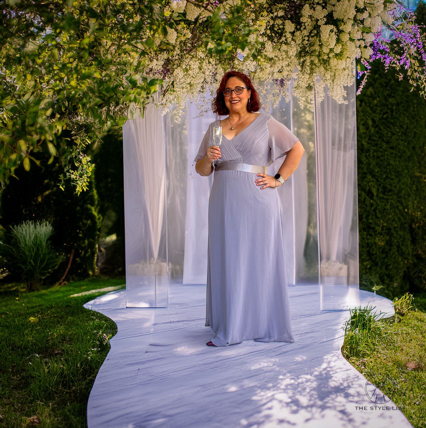 A woman in a long grey dress is holding a glass of wine.